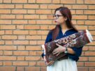 A woman holding a large pillow in front of a brick wall