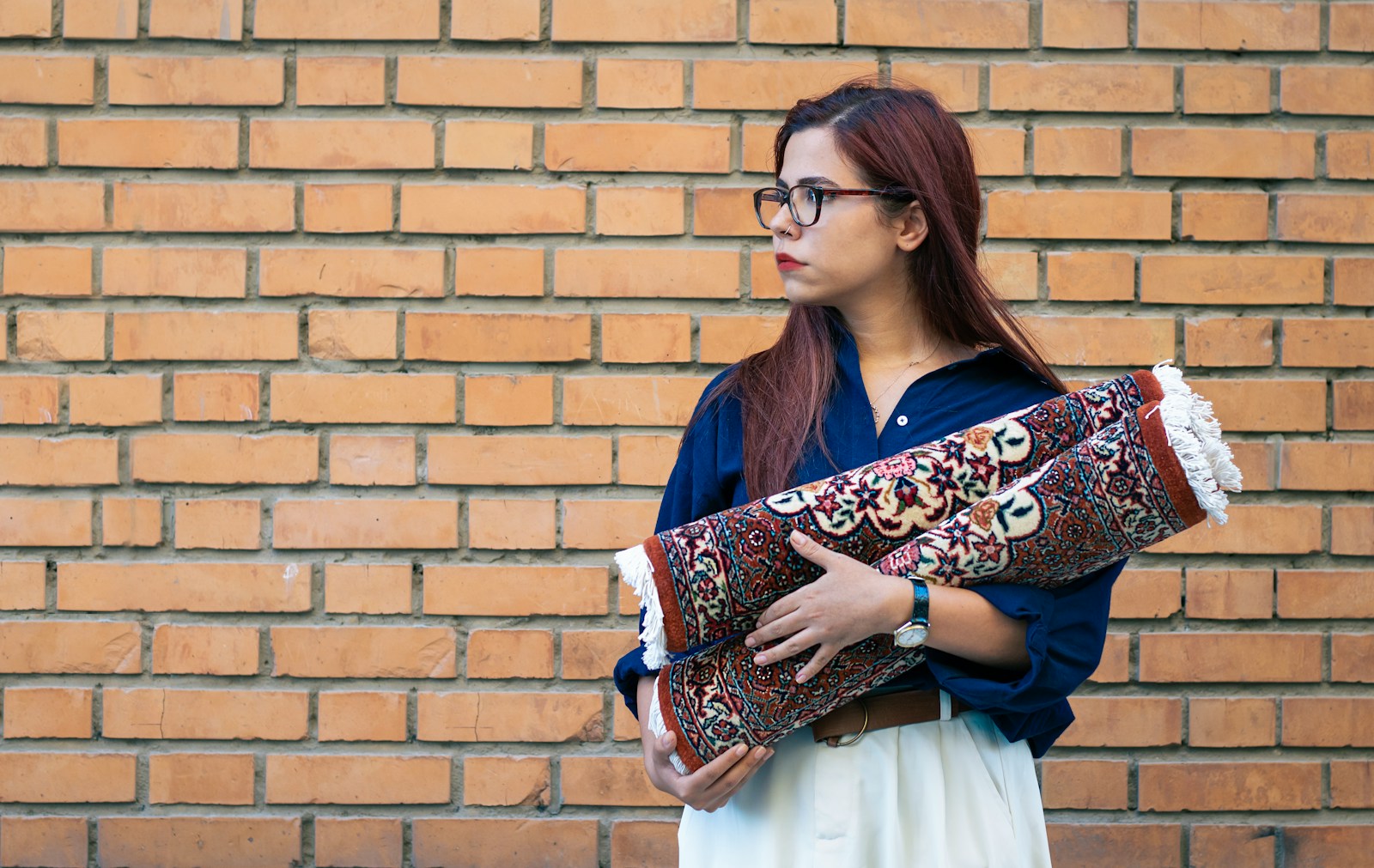 A woman holding a large pillow in front of a brick wall